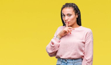 Dudaklarında parmak ile sessiz olmanı izole arka plan üzerinde kazak giyen genç örgülü saç Afrikalı-Amerikalı kız. Sessizlik ve gizli kavramı.