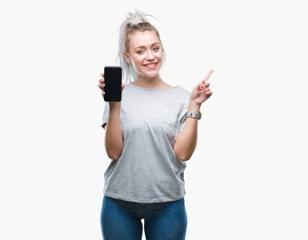 年轻的金发碧眼的女人显示在孤立的背景智能手机屏幕非常高兴用手和手指指向一边 — 图库照片