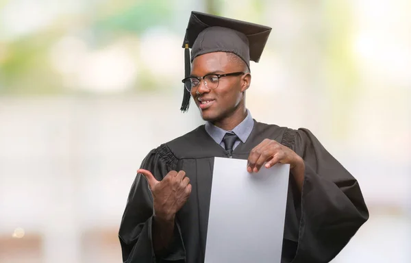 ヤング卒業したアフリカ系アメリカ人を指していると幸せそうな顔を笑顔で側まで親指で示す分離の背景に白紙の学位を保持 — ストック写真