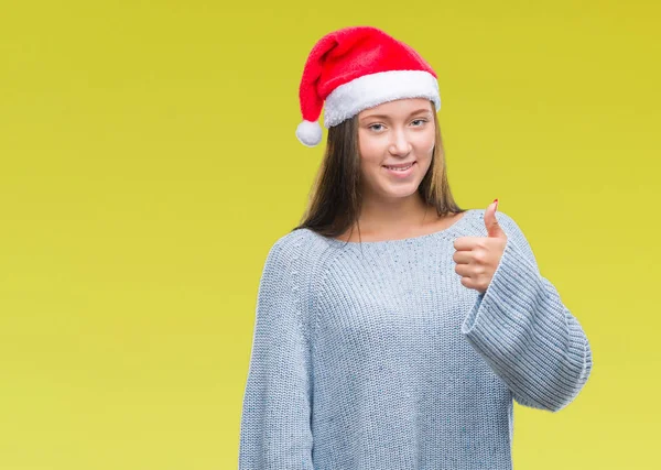 年轻美丽的高加索妇女戴着圣诞帽在孤立的背景做快乐的大拇指与手的手势 通过显示成功来批准镜头的表达 — 图库照片