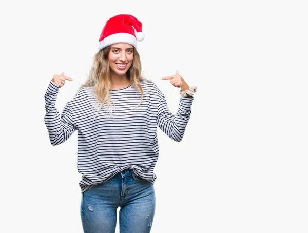 孤立した背景の顔に笑顔と自信を持って 誇りと幸せな指で自分を指して上クリスマス帽子身に着けている美しい若いブロンドの女性 — ストック写真