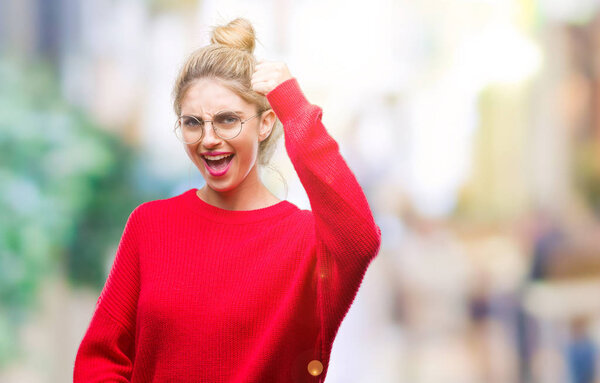 Young beautiful blonde woman wearing red sweater and glasses over isolated background angry and mad raising fist frustrated and furious while shouting with anger. Rage and aggressive concept.
