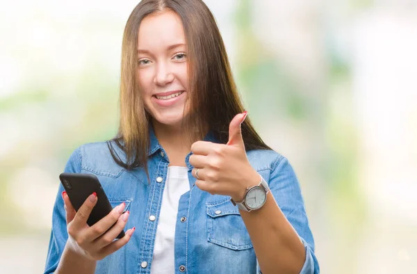年轻美丽的白种人妇女短信发送消息使用智能手机在孤立的背景快乐与大微笑做 拇指与手指 优秀的标志 — 图库照片