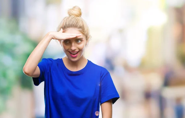 Young beautiful blonde and blue eyes woman wearing blue t-shirt over isolated background very happy and smiling looking far away with hand over head. Searching concept.