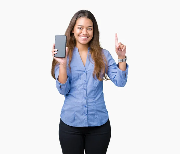 年轻美丽的黑发女商人显示智能手机屏幕在孤立的背景惊讶的想法或问题用快乐的脸指指点点 — 图库照片