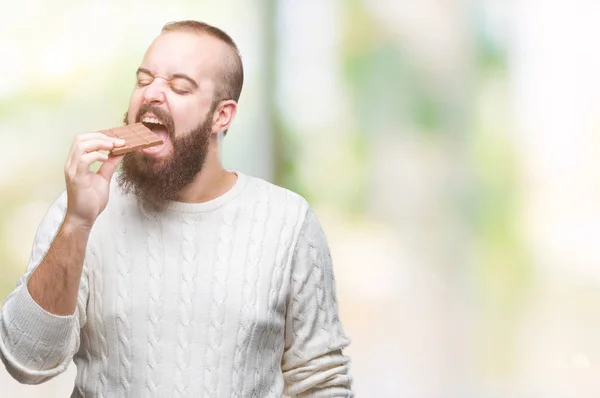 年轻的嬉皮士男子吃巧克力棒在孤立的背景与自信的表情在聪明的脸上思考严肃 — 图库照片