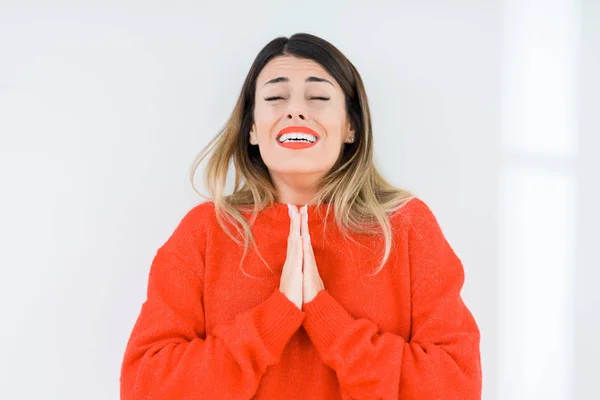 Young woman wearing casual red sweater over isolated background begging and praying with hands together with hope expression on face very emotional and worried. Asking for forgiveness. Religion concept.