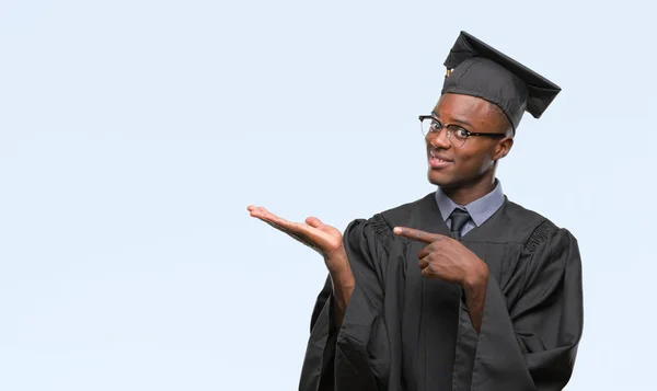 Young graduated african american man over isolated background amazed and smiling to the camera while presenting with hand and pointing with finger.