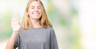 Büyük boy rahat t-shirt üzerine izole arka plan Waiving Merhaba mutlu ve gülümseyen, dostça karşılama jest giyen güzel genç kadın