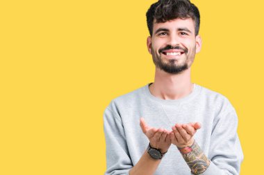 Genç yakışıklı adam giyen kazak izole üzerinden alma veya jest vererek birlikte el avuç içi ile gülen arka plan. Ayrı tutma ve koruma