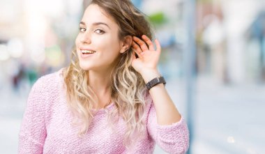 Güzel sarışın genç kadın bir işitme söylenti ya da dedikodu için dinleme kulak üzerinde el ile gülümseyen izole arka plan üzerinde. Sağırlık kavramı.