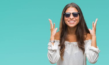 Genç güzel Arap kadın deli ve çığlık kaldırdı ve kapalı gözleri heyecanlı silah ile başarı için deli kutluyor izole arka plan üzerinde güneş gözlüğü takıyor. Kazanan kavramı