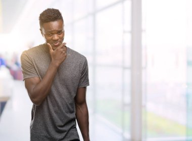 Emin çapraz kollar ve çeneme kaldırdı el ile gülümseme ile kamera seyir gri t-shirt giyen genç Afro-Amerikan adam. Pozitif düşünce.