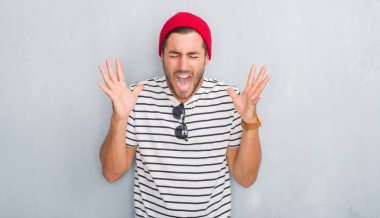 Yakışıklı genç hippi erkek lacivert t-shirt ve yün kap kutlama kızgın ve silah ile başarı için deli gri grunge duvarın üzerinden kaldırdı ve heyecanlı çığlık gözler kapalı. Kazanan kavramı