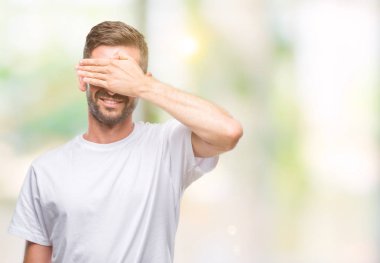 Yakışıklı genç gülümseyen ve gözler için sürpriz kapsayan yüz el ile gülüyor izole arka plan üzerinde. Kör kavramı.