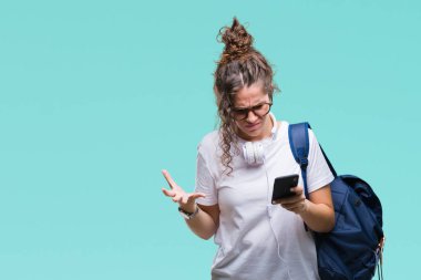 Sırt çantası, kulaklık ve akıllı telefon üzerinde izole giyen genç esmer öğrenci kız arka plan ile öfke, çılgın ve yükseltilmiş eliyle diye bağıran rahatsız ve hayal kırıklığına uğramış öfke kavramı bağırarak