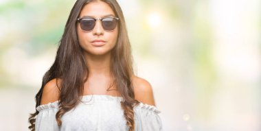 Genç güzel Arap kadın yüzünde ciddi bir ifade ile izole arka plan üzerinde güneş gözlüğü takıyor. Basit ve doğal kameraya bakıyor.