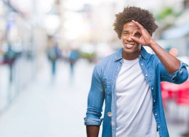 Afro Amerikalı adam gülümsüyor, parmakları ile mutlu yüz üzerinden seyir göz el ile ok jest yapıyor izole arka plan üzerinde.