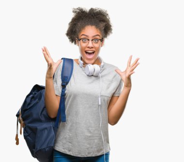 Üzerinde kulaklık ve sırt çantası giyen genç afro Amerikan öğrenci kadın deli kutluyor arka plan izole ve çığlık kaldırdı ve açık gözleri heyecanlı silah ile başarı için hayrete düşürdü. Kazanan kavramı