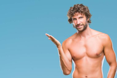 Yakışıklı İspanyol modeli adam seksi ve neşeli sunulması ve kameraya bakarak avucunun ile işaret gülümseyen izole arka plan üzerinde gömleksiz.