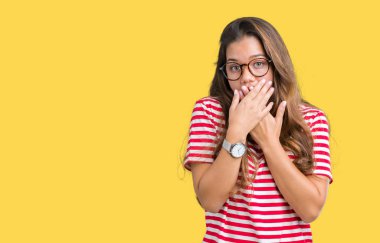 Giyen genç güzel esmer kadın gözlük ve t-shirt izole arka plan ağız hata için elleriyle kapsayan şok üzerinde çizgili. Gizli kavramı.