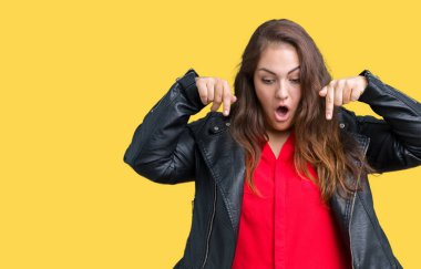 Artı boyutu genç kadın izole arka plan üzerinde bir moda deri ceket giymiş güzel aşağı işaret parmaklarıyla reklam, gösterilen yüz şaşırttı ve ağzı açık