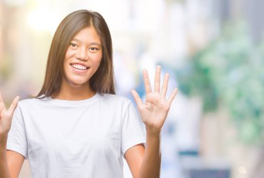 Genç Asyalı kadın gösterilen ve parmakları ile işaret izole arka plan üzerinde kendinden emin ve mutlu gülümseyerek süre yedi numara.