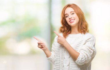 İzole arka plan gülümseyen ve iki elleri ve parmakları ile tarafına işaret kamera bakarak kış kazak giyen genç güzel kadın.