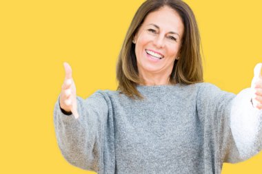 Sarılmak için kollarını açarak gülümseyerek kameraya bakarak izole arka plan üzerinde kış kazak giyen güzel orta yaş kadın. Neşeli ifade kucaklayan mutluluk.