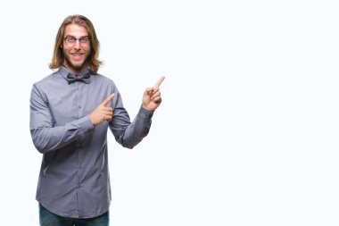 Gülümseyen ve iki elleri ve parmakları ile tarafına işaret kamera bakarak izole arka plan üzerinde papyon giyiyor uzun saçlı yakışıklı delikanlı.