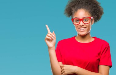 Kameraya bakarak yan el ve parmak ile işaret yüzünde kocaman bir gülümseme ile izole arka plan üzerinde gözlük takan genç afro Amerikalı kadın.