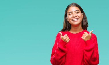 El ile pozitif jest yapıyor izole arka plan başarı işareti üzerinde kış kazak giyen genç güzel Arap kadın başparmak gülümseyen ve mutlu. Neşeli bir ifadeyle, kazanan jest kameraya bakıyor.