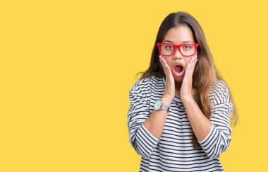 Giyen genç güzel esmer kadın kazak ve kırmızı gözlük korkuyor ve şok sürpriz ifade, korku ve heyecan yüz ile izole arka plan üzerinde çizgili.