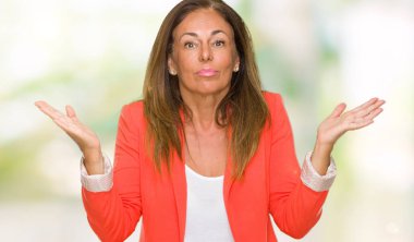 Güzel orta yaş iş izole arka plan clueless ve şaşkın bir ifadeyle kollar ve eller kaldırdı yetişkin kadın. Şüphe kavramı.