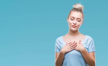 Sarışın genç kadın ile gülümseyen izole arka plan üzerinde kapalı gözler ve yüzünde minnettar jest ile göğüs üzerinde eller. Sağlık kavramı.