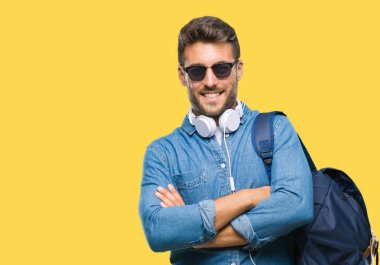 Üzerinde kulaklık ve sırt çantası giyen genç yakışıklı turist adam mutlu yüz ile gülümseyerek kameraya seyir silah geçti arka plan izole. Olumlu bir kişi.