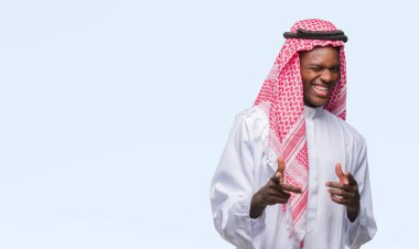 Geleneksel keffiyeh fotoğraf makinesi ile mutlu ve komik yüz için parmakları işaret izole arka plan üzerinde giyen genç Arapça Afrika adam. İyi enerji ve vibes.