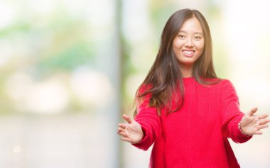 Sarılmak için kollarını açarak gülümseyerek kameraya bakarak izole arka plan üzerinde kış kazak giyen genç Asyalı kadın. Neşeli ifade kucaklayan mutluluk.