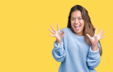 Üzerinde mavi kış kazak giyen genç güzel esmer kadın deli kutluyor arka plan izole ve başarı için kaldırdı kollarını açarak hayrete ve heyecanlı çığlık gözleri açık. Kazanan kavramı