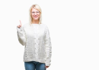 Kış kazak ve gözlük ve parmak gülümseyen süre bir numara ile kendinden emin ve mutlu yukarıyı gösteren izole arka plan üzerinde giyen genç güzel sarışın kadın.