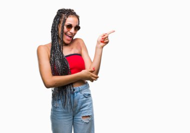 Kameraya bakarak yan el ve parmak ile işaret yüzünde kocaman bir gülümseme ile izole arka plan üzerinde güneş gözlüğü takıyor Doğum işareti ile genç örgülü saç Afrikalı-Amerikalı.