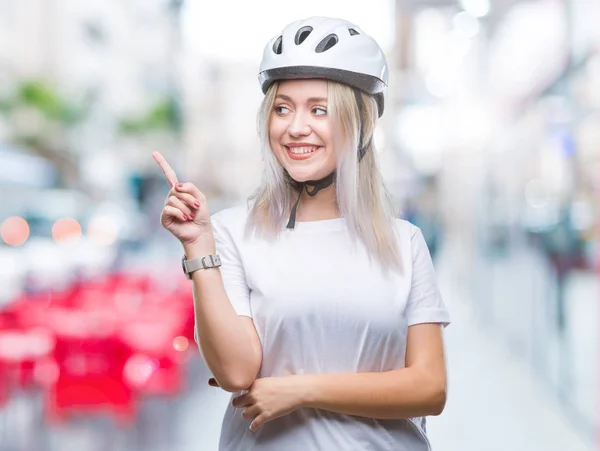 年轻的金发碧眼的女子戴着自行车安全头盔 脸上带着灿烂的笑容 用手和手指指着一旁看着镜头 — 图库照片