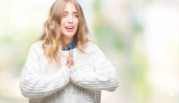 Beautiful young blonde woman wearing winter sweater over isolated background begging and praying with hands together with hope expression on face very emotional and worried. Asking for forgiveness. Religion concept.