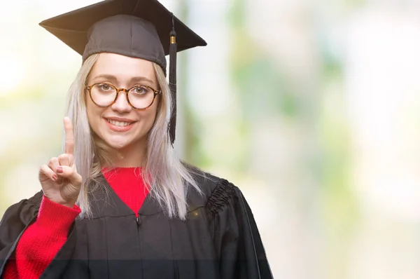 年轻的金发碧眼的女人穿着研究生制服在孤立的背景显示和指向手指第一 同时微笑着自信和快乐 — 图库照片