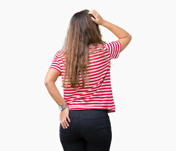 年轻美丽的黑发女人穿着条纹 T恤在孤立的背景向后思考怀疑与手在头 — 图库照片