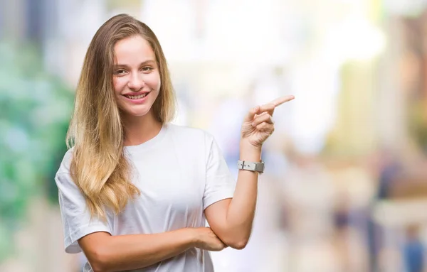 年轻美丽的金发碧眼的女人穿着休闲的白色 T恤在孤立的背景与一个很大的微笑在脸上 用手和手指指着一边看着镜头 — 图库照片