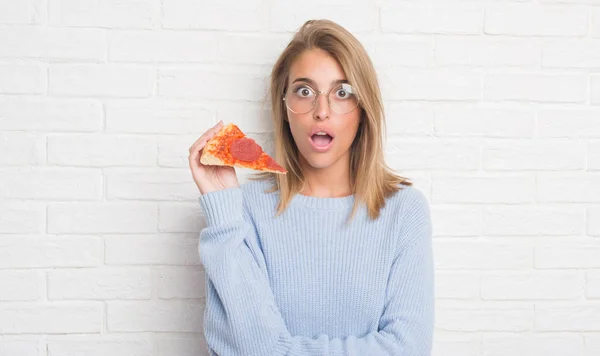 Hermosa Joven Sobre Pared Ladrillo Blanco Comiendo Rebanada Pizza Asustada — Foto de Stock