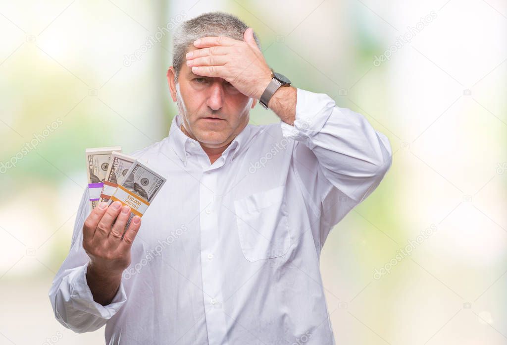 Handsome senior man holding bunch of money over isolated background stressed with hand on head, shocked with shame and surprise face, angry and frustrated. Fear and upset for mistake.