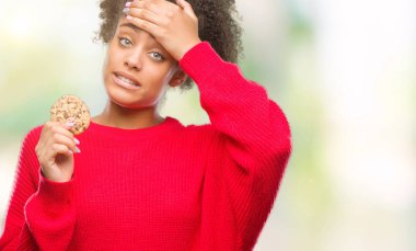 Genç afro Amerikalı kadın baş, el ile vurguladı izole arka plan üzerinde çikolatalı kurabiye yemek şok utanç ve sürpriz suratla, öfkeli ve sinirli. Korku ve hata için üzgün.