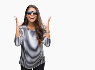 Genç güzel Arap kadın deli ve çığlık kaldırdı ve kapalı gözleri heyecanlı silah ile başarı için deli kutluyor izole arka plan üzerinde güneş gözlüğü takıyor. Kazanan kavramı